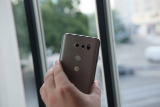 Hand holding LG V30 smartphone by window with city view.