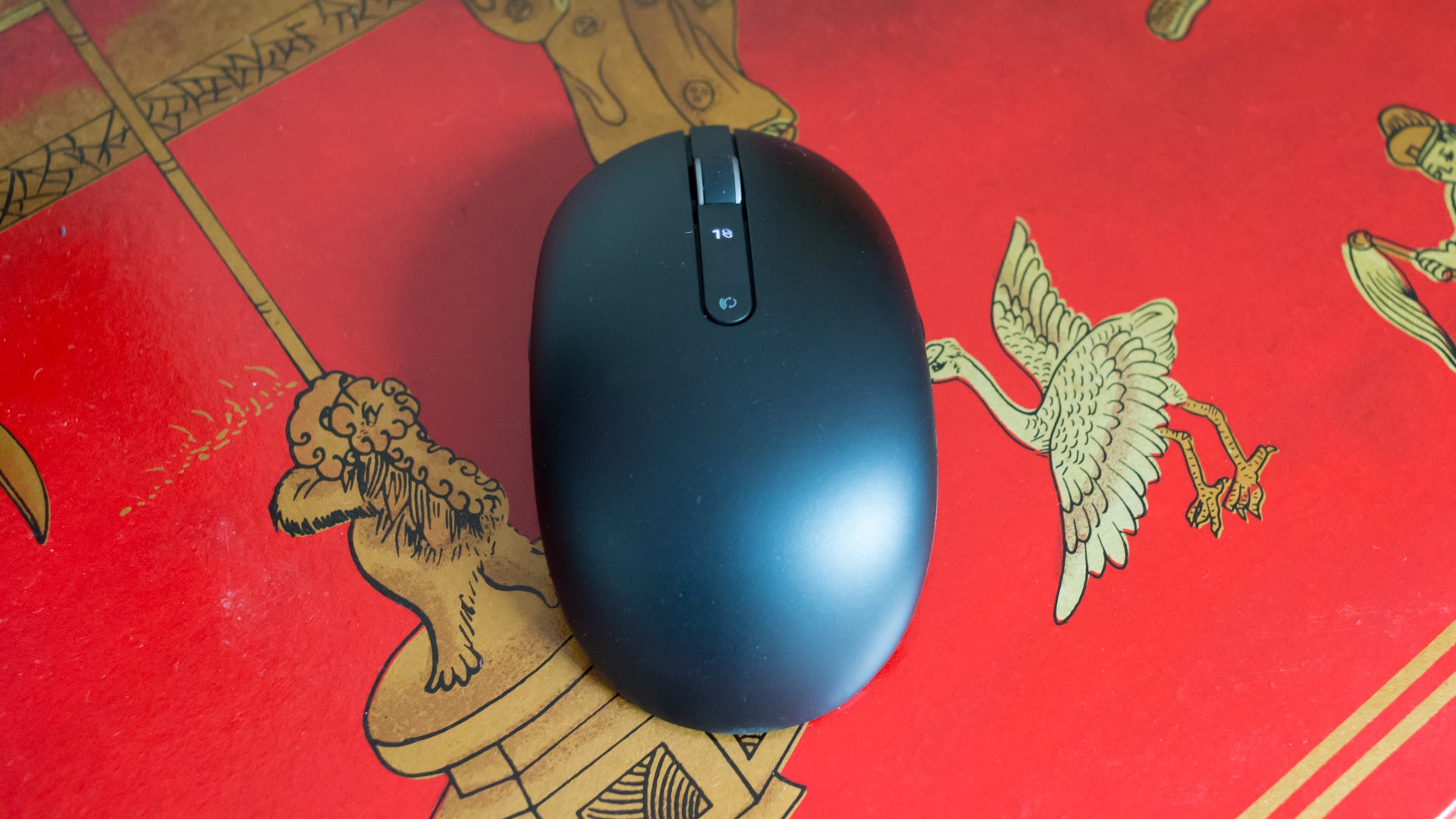 Black wireless mouse on a red patterned surface.