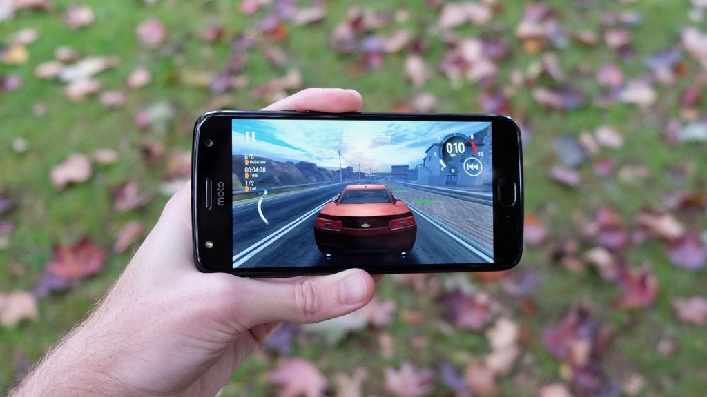 Hand holding Moto X4 displaying a car racing game.