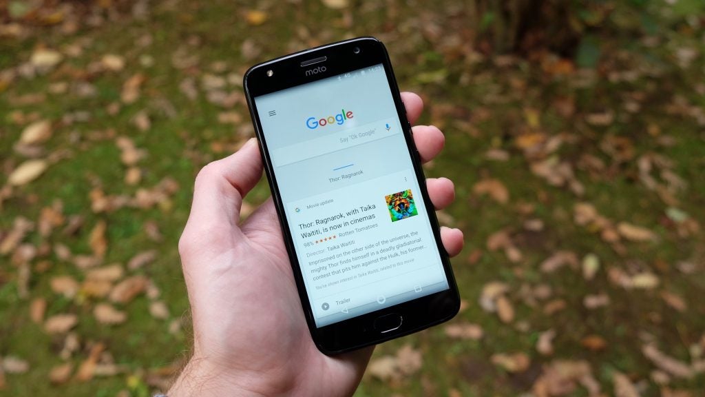 Hand holding Moto X4 displaying a Google search result.