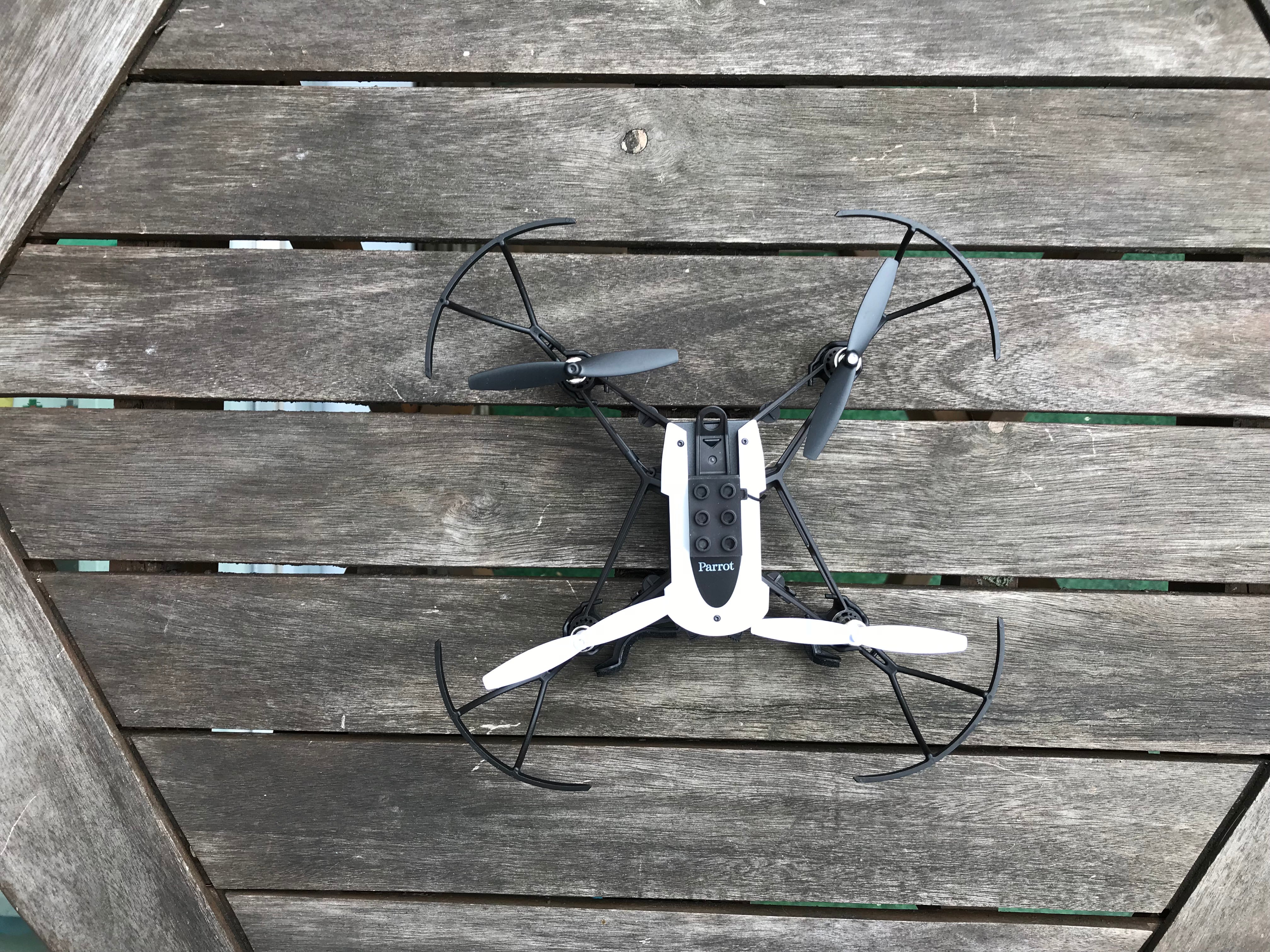 Parrot Mambo drone with propeller guards on wooden deck.