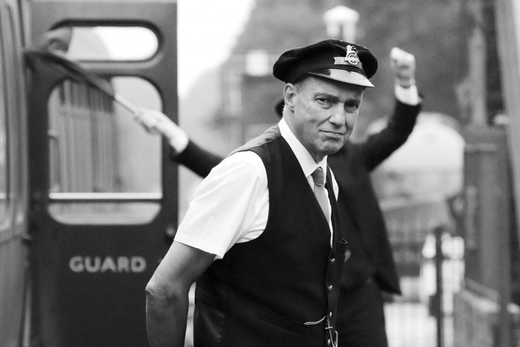 Train conductor signaling departure in black and white photo.