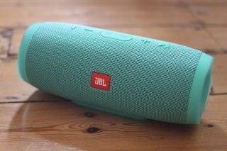 JBL Charge 3 portable speaker in teal on wooden surface.
