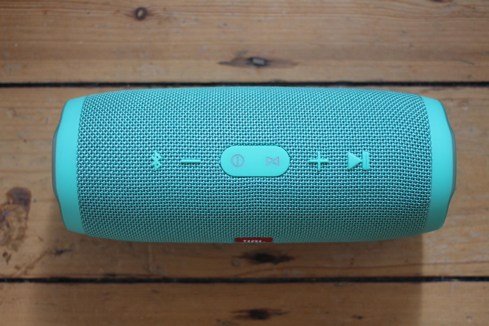 JBL Charge 3 portable speaker in teal on wooden background.