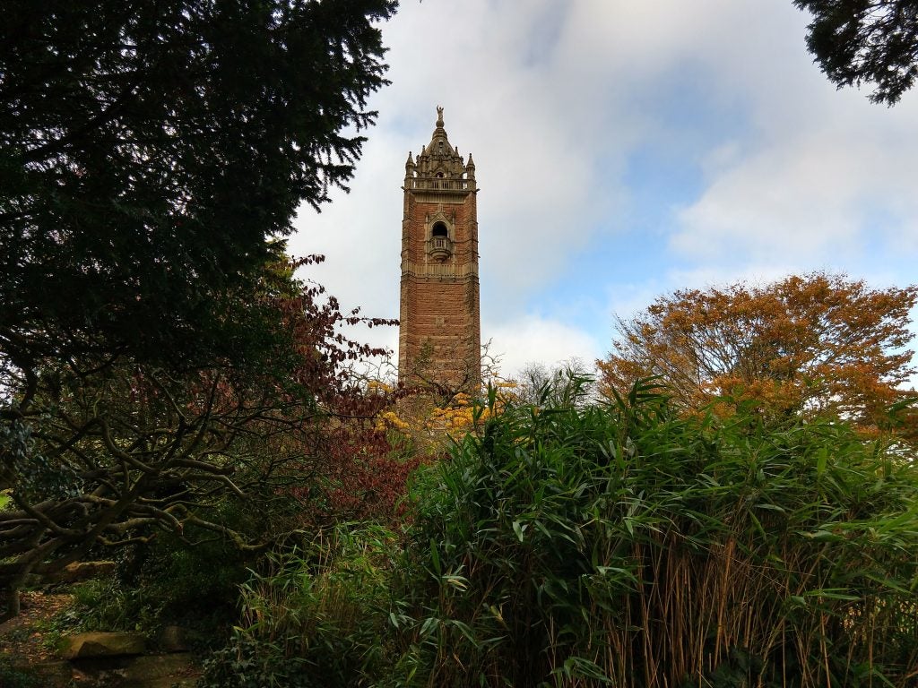 Stone tower rising above autumn foliage against a cloudy sky.