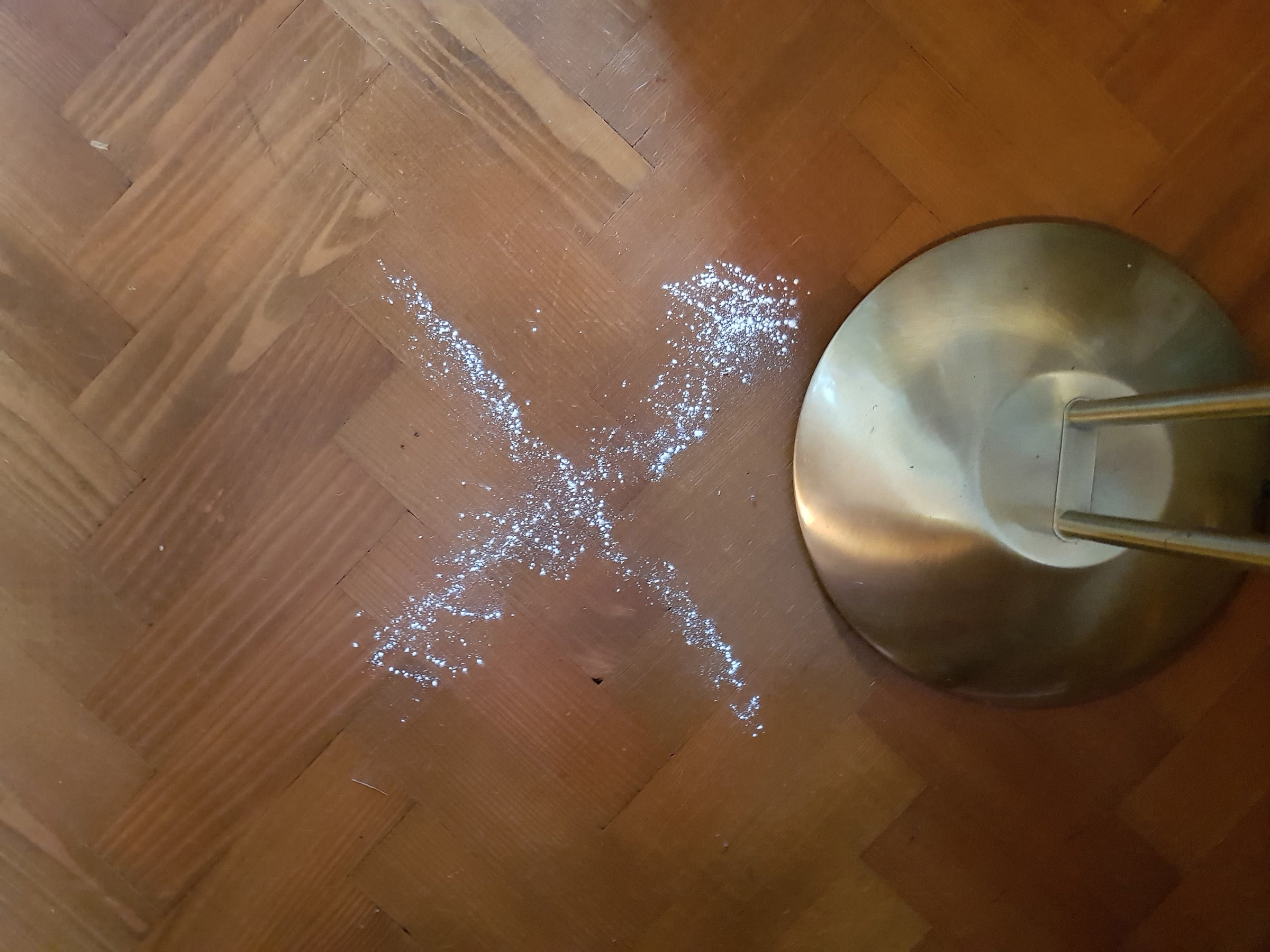 Spilled sugar next to a lamp on a wooden floor.