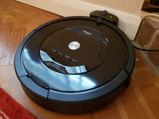 iRobot Roomba 875 vacuum cleaning hardwood floor near fireplace.