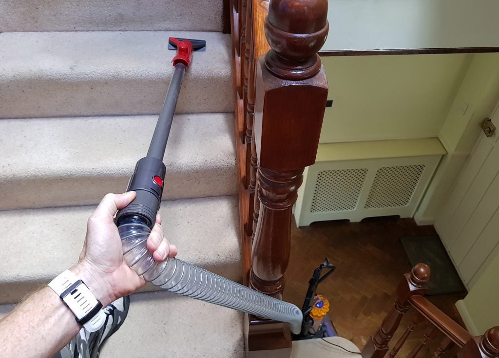 Dyson vacuum being used on staircase with attachment.