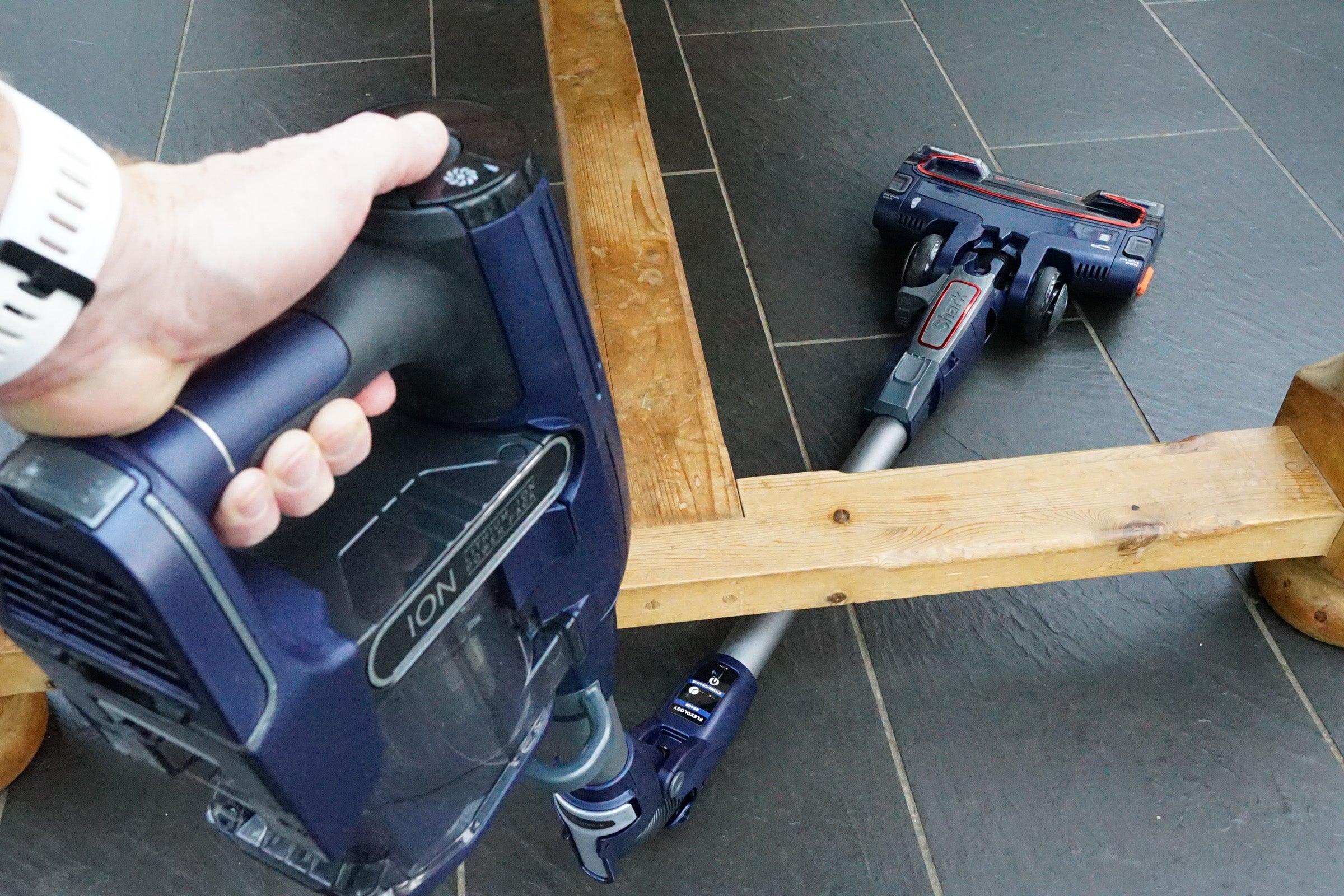Hand holding a Shark DuoClean Cordless vacuum part with main unit in background.