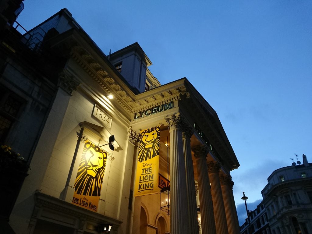 Low-light photo of a theater entrance advertising The Lion King.Low light city street scene captured with high detail and clarity.Historic church building exterior with trees and lawn.