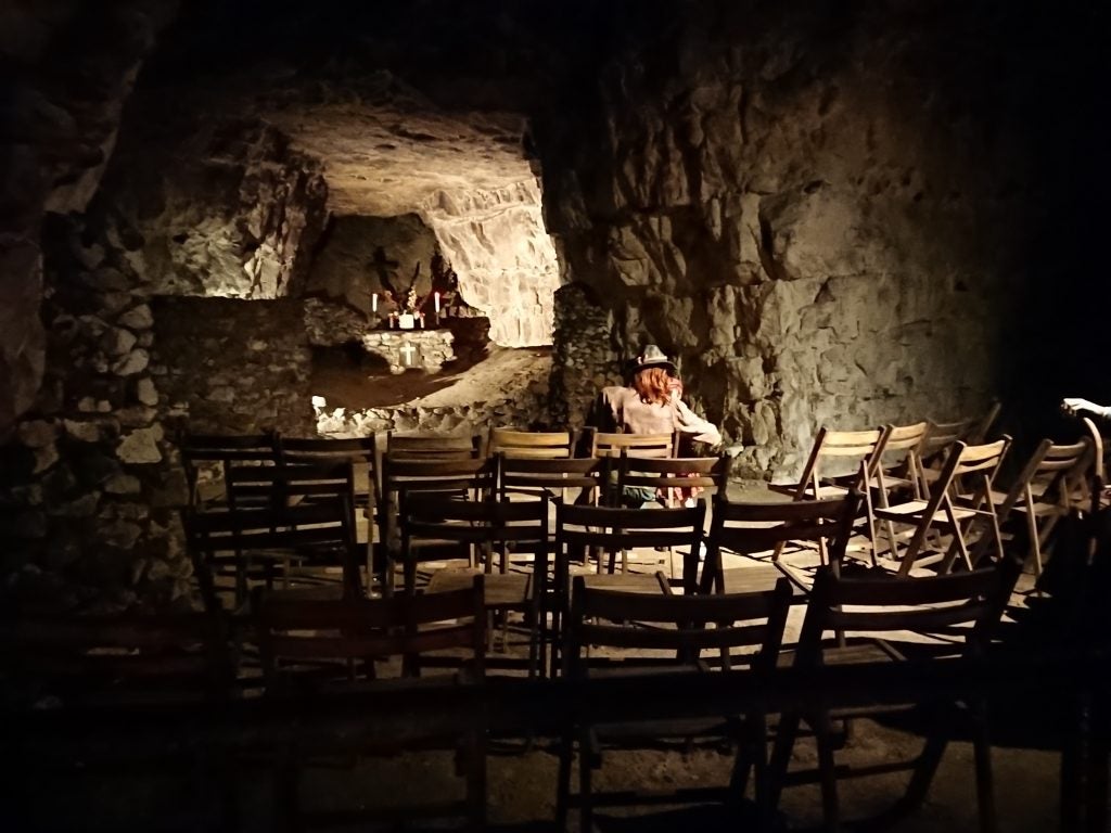 Low-light photo of a cave with seating area and person.