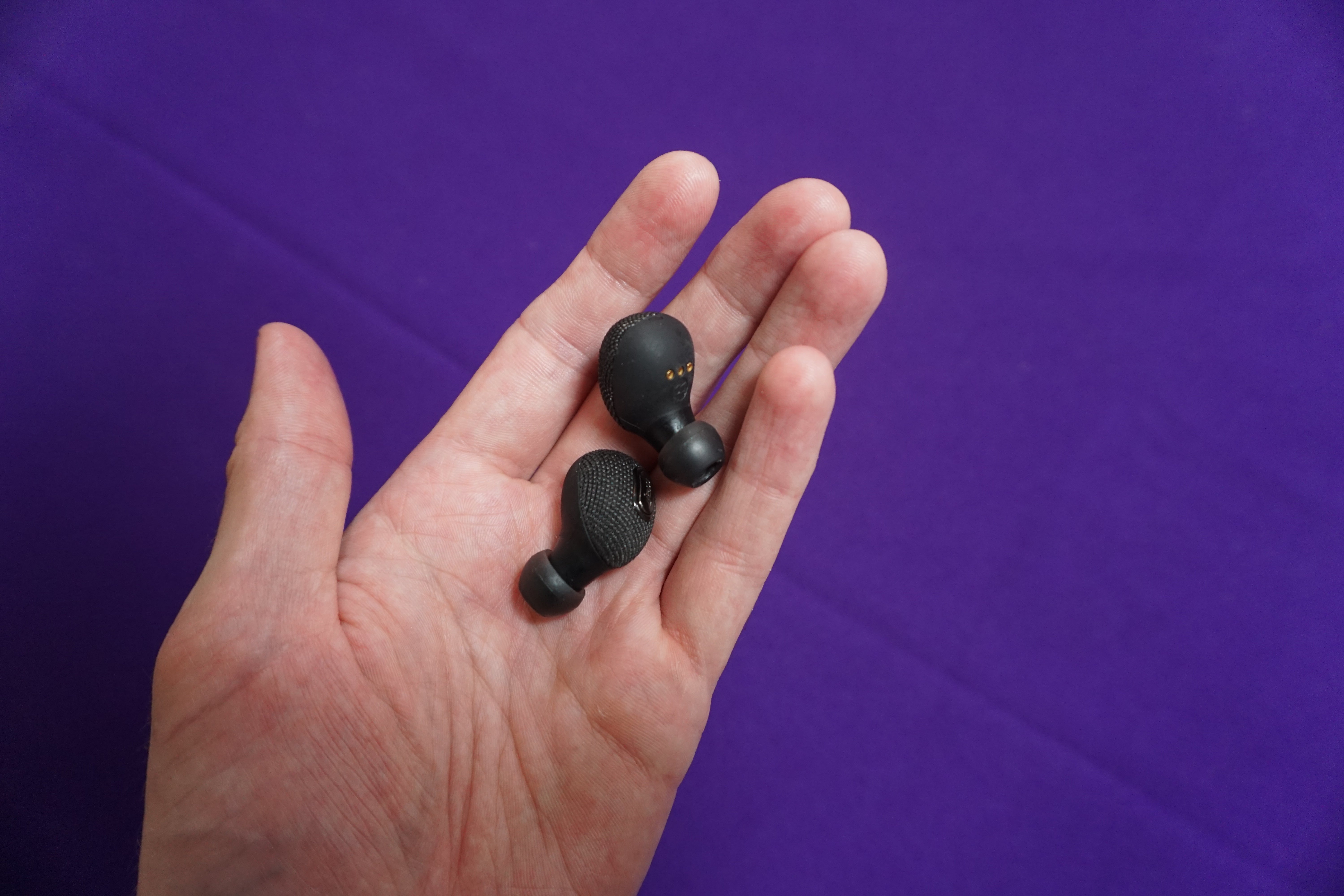 Hand holding Jam Ultra wireless earbuds on purple background