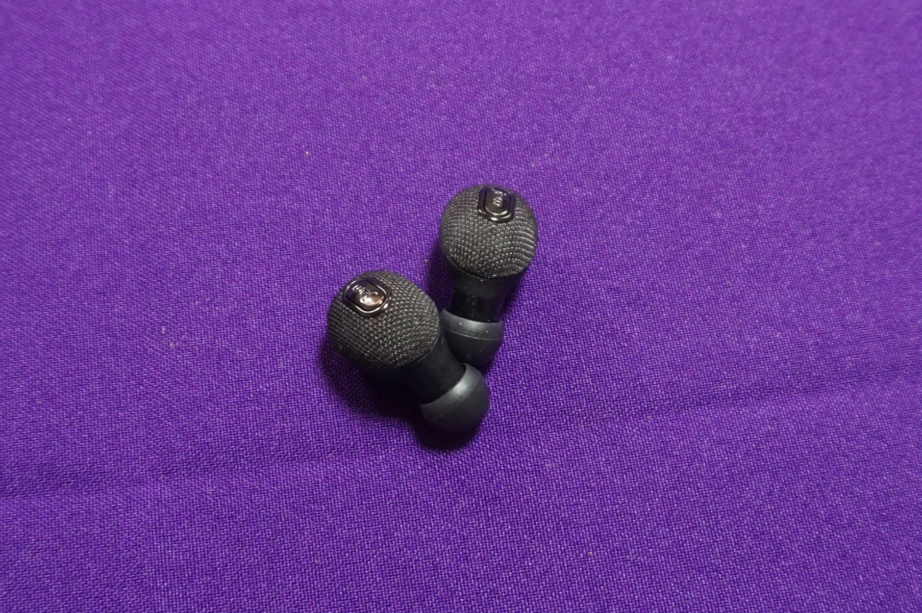 Jam Ultra wireless earbuds on purple fabric background