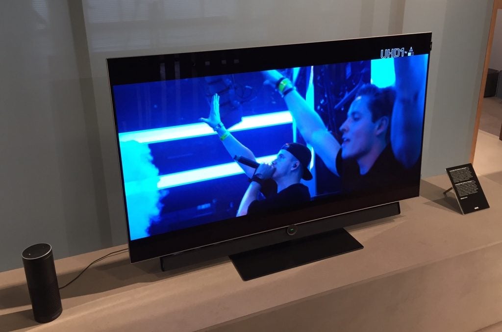 Loewe Bild OLED TV displaying concert scene on screen with external speaker.