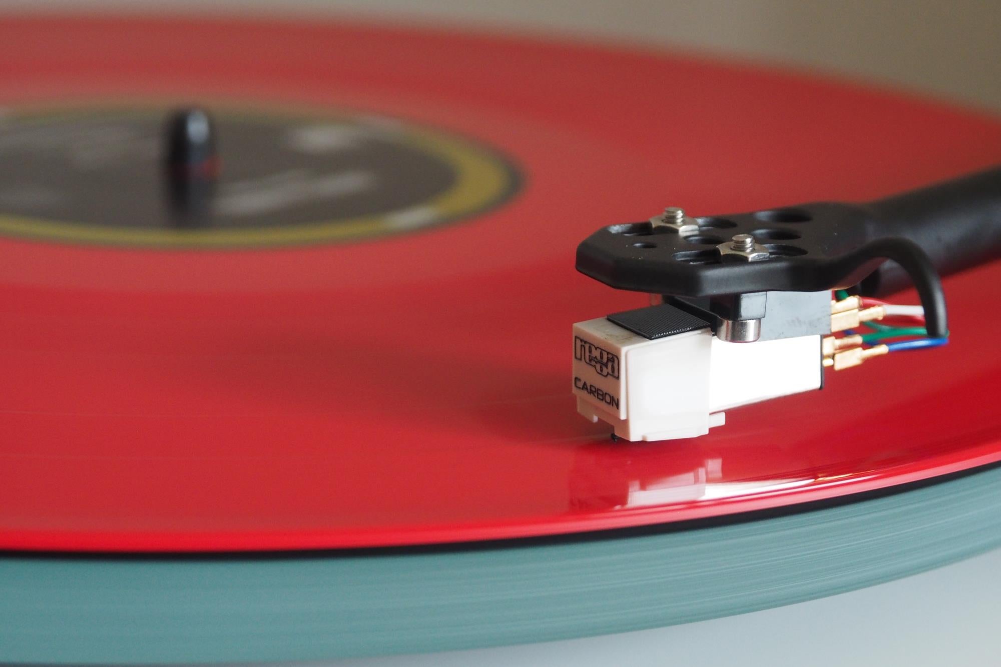 Close-up of Rega Planar 2 turntable needle on red vinyl record.