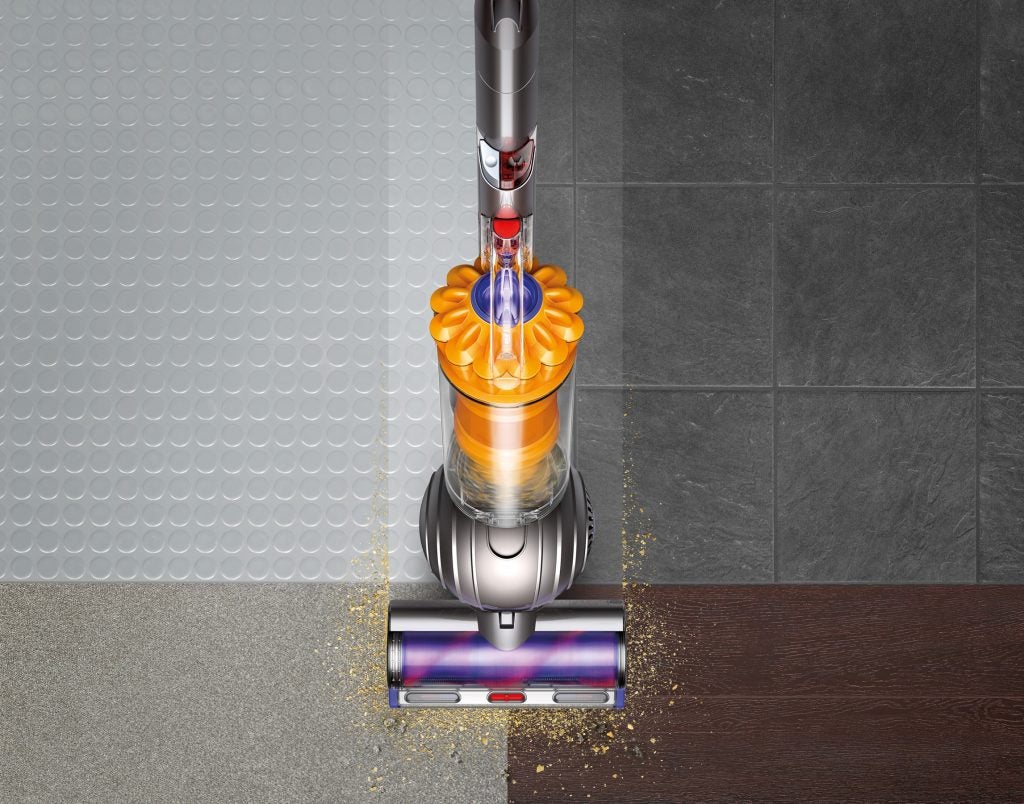 Dyson vacuum cleaner on mixed flooring with visible debris.