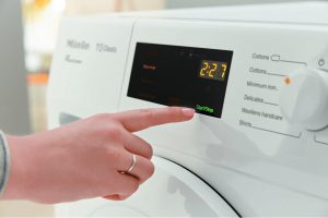 Person pressing start button on Miele TDB120WP dryer control panel.
