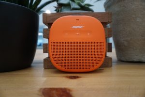 Bose SoundLink Micro speaker in orange on wooden stand.