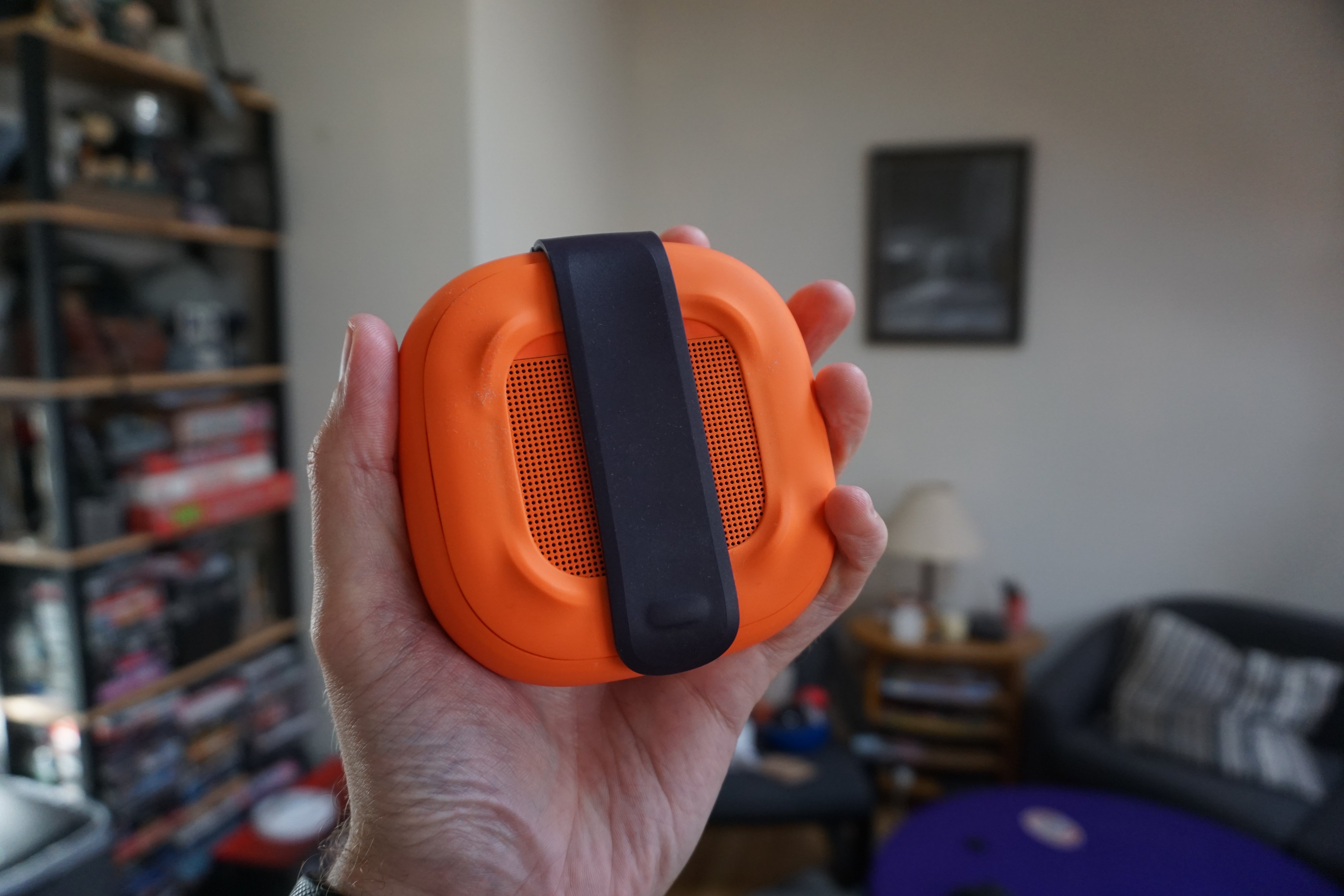 Hand holding an orange Bose SoundLink Micro speaker.