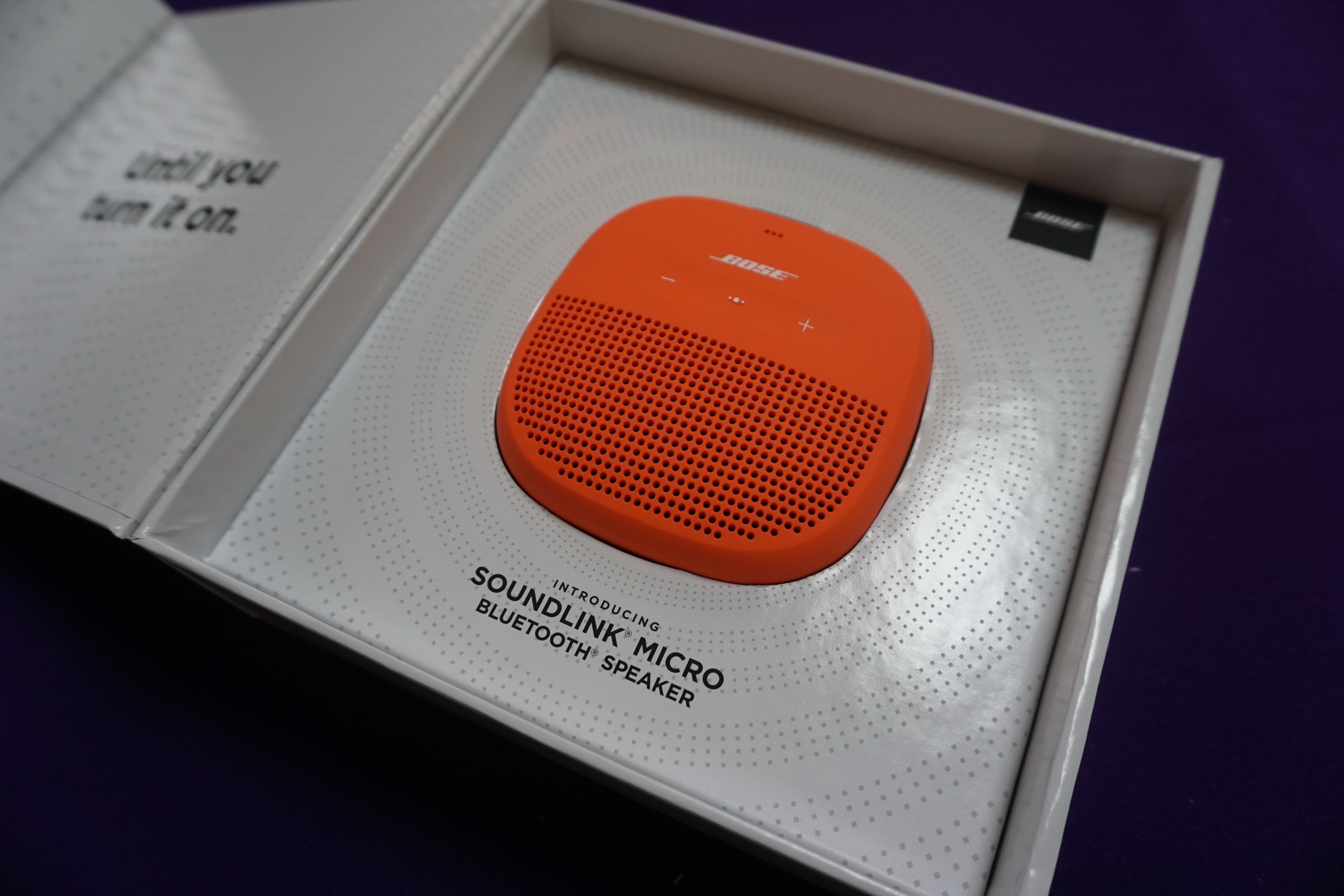 Bose SoundLink Micro speaker in orange in its box.