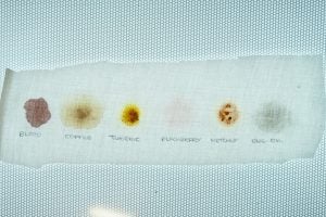 Stain removal test results on white fabric with annotations.