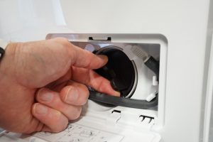 Hand examining the filter compartment of LG washing machine.