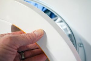 Hand opening a white Miele TDB120WP tumble dryer door.