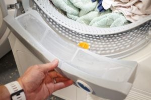 Hand removing lint filter from Miele dryer with laundry inside.