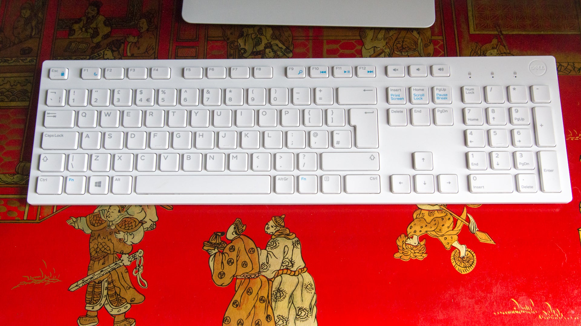 Dell white wireless keyboard on a red patterned desk.
