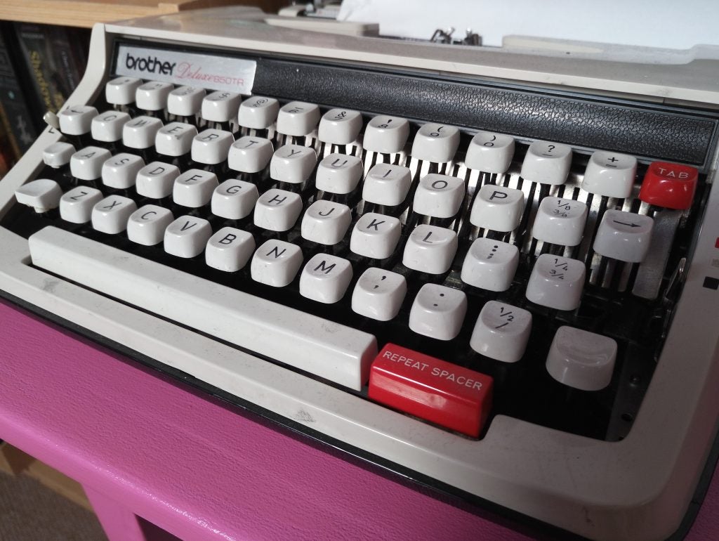 Vintage Brother Charger 11 typewriter on a pink desk.Assorted children's books on a white shelf.