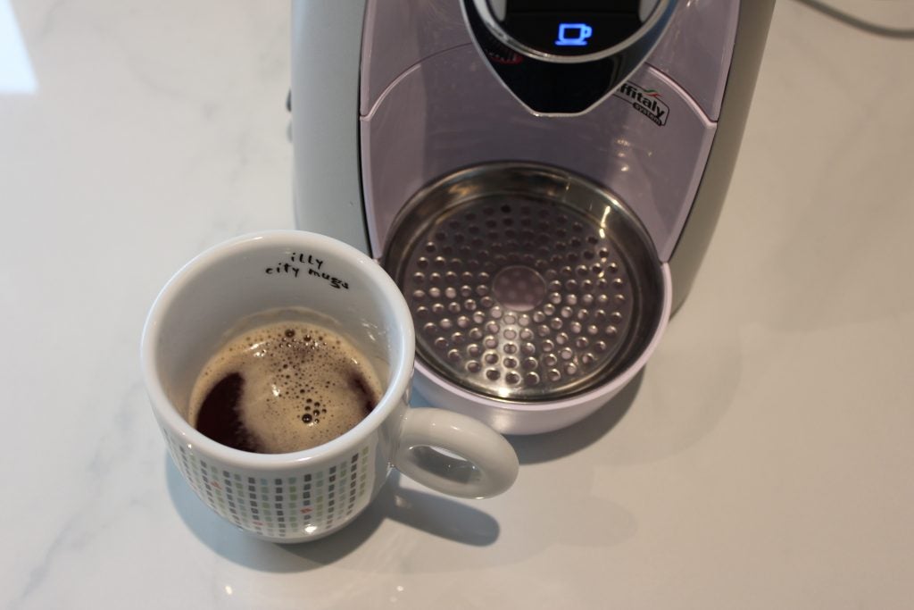 Espresso cup with coffee next to SO4 capsule machine.