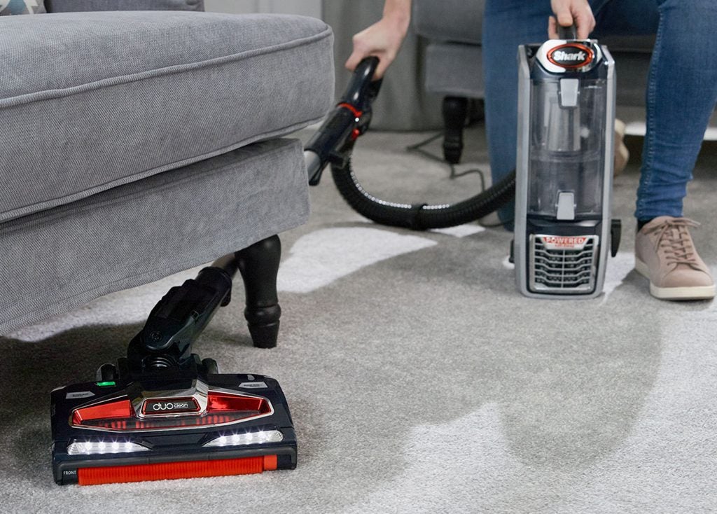 Shark DuoClean vacuum being used on carpet near sofa.