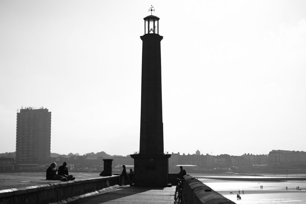Monochrome image of people by a lighthouse and building