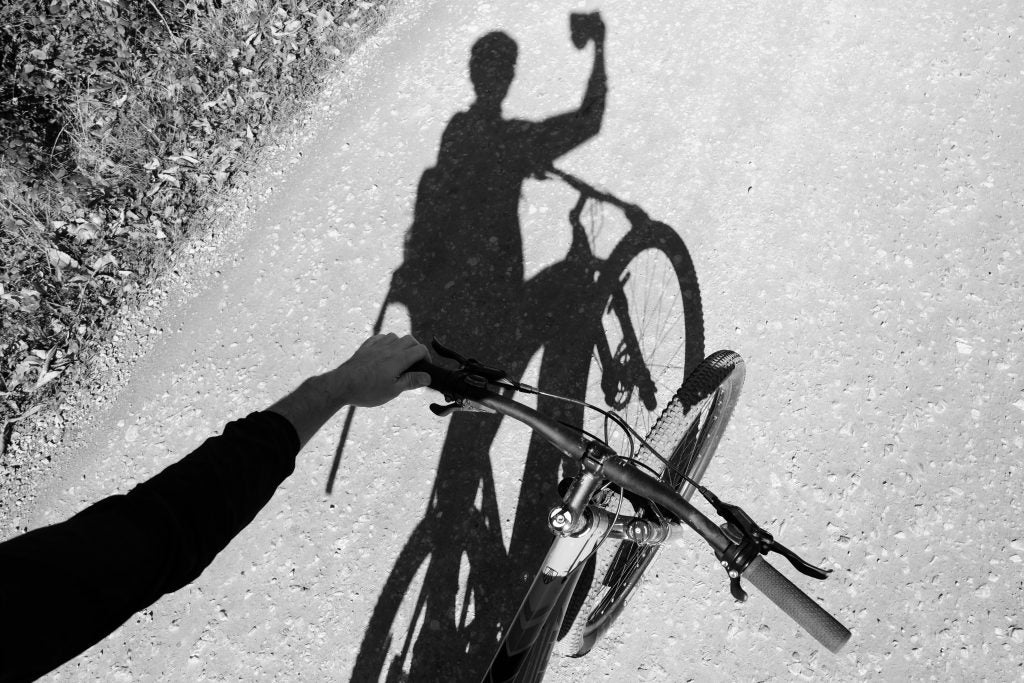Cyclist's shadow on ground while holding up a camera.