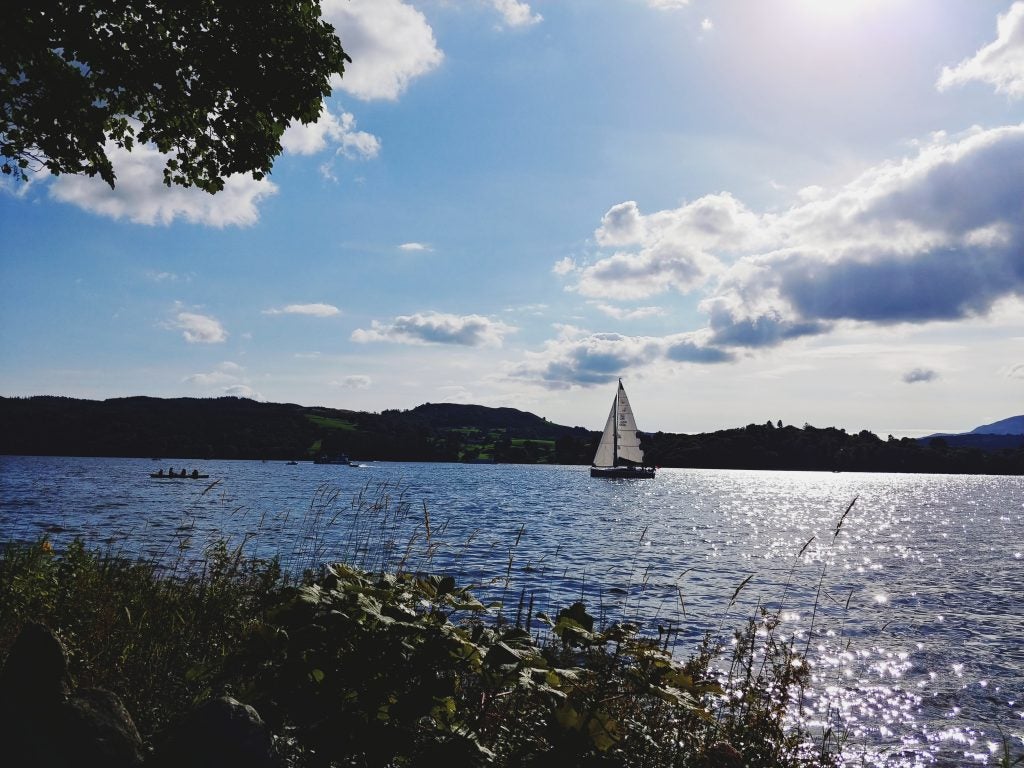 Sailboat and rowers on a lake with sparkling water and clouds.
