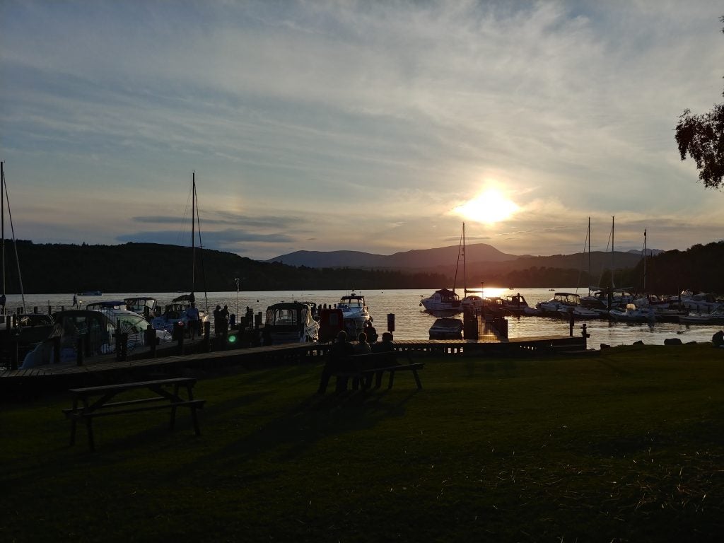 Sunset view over a lake with boats and mountains in background.