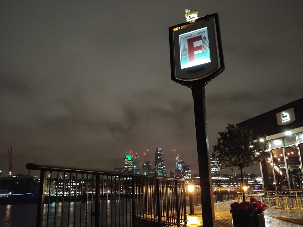 Nighttime cityscape photo with illuminated pub sign in foreground.