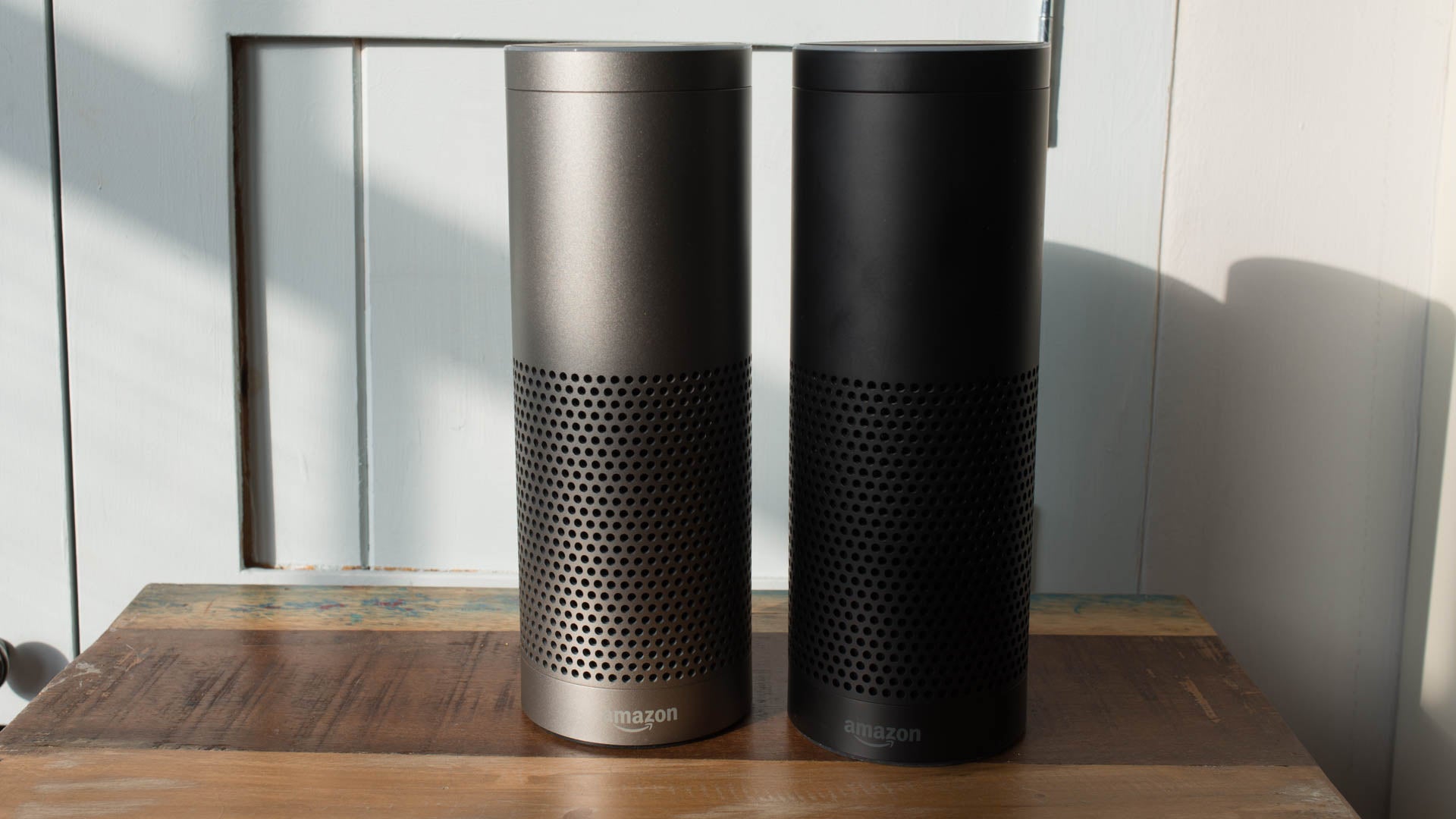 Silver and black Amazon Echo Plus devices on wooden table.