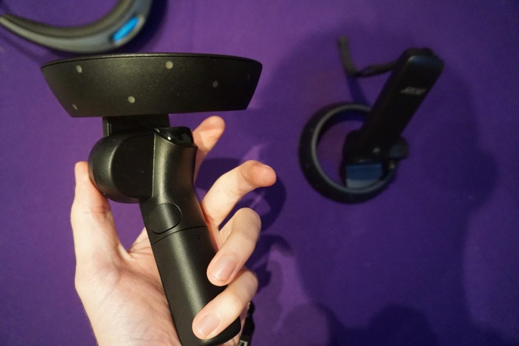 Hand holding a Windows Mixed Reality controller with headset in background.