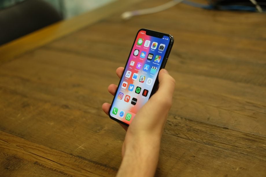 Hand holding an iPhone X displaying the home screen.