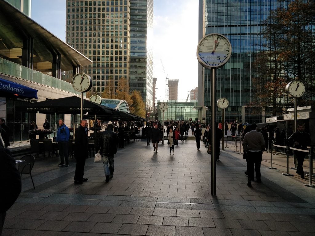 Crowded pedestrian area with multiple clocks and skyscrapers.