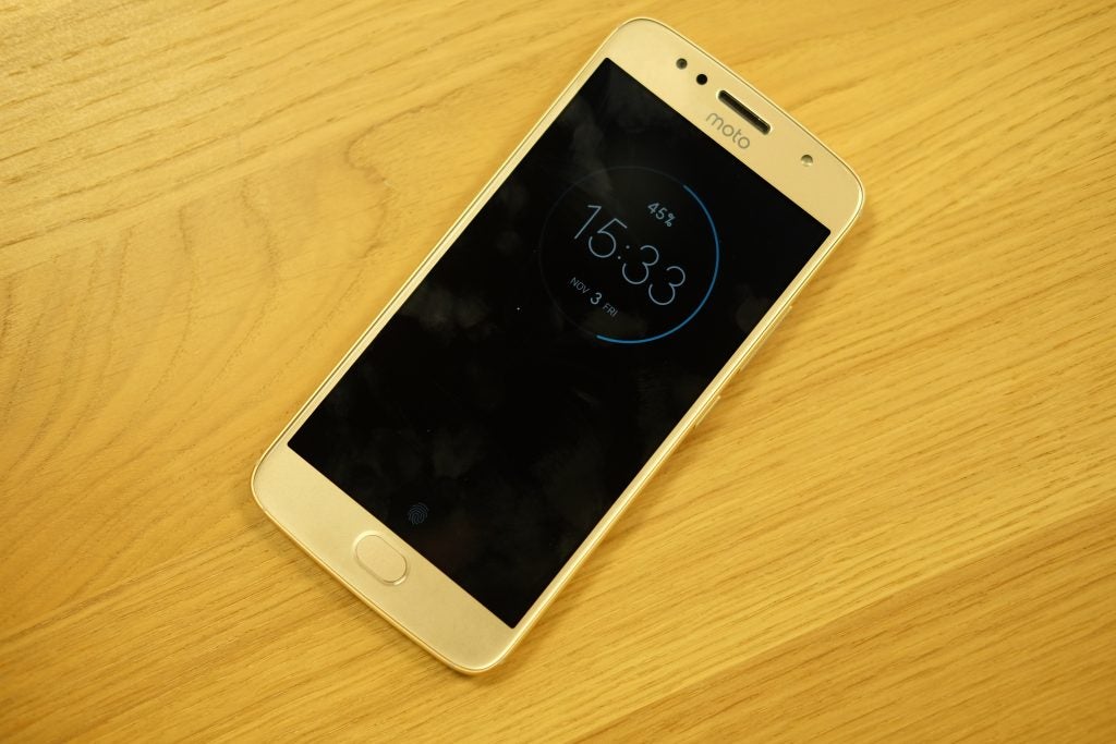 Moto G5S smartphone on wooden surface with clock display.