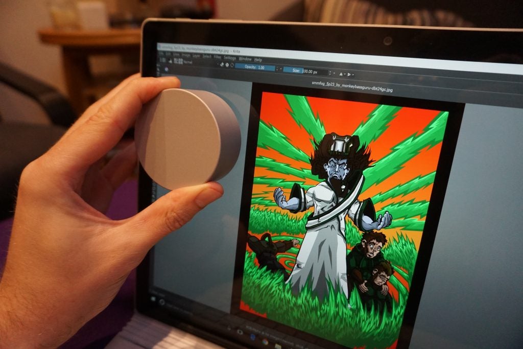 Hand using dial on Surface Book 2 displaying digital artwork.