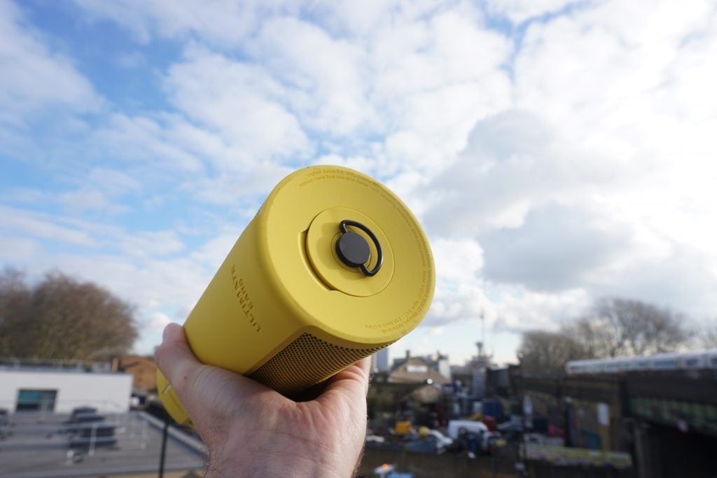 Hand holding yellow UE Megablast portable speaker outdoors.