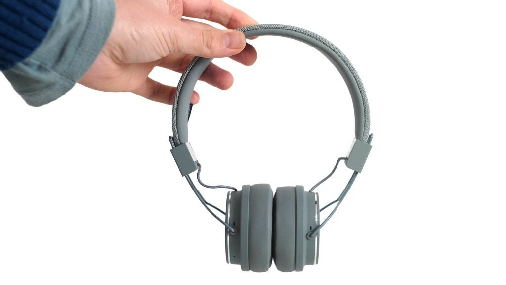 Hand holding Urbanears Plattan 2 Bluetooth headphones against a white background.