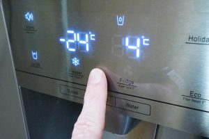 Finger pressing digital temperature control on Hisense fridge-freezer