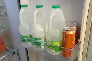 Milk bottles and soda cans inside a fridge door shelf.
