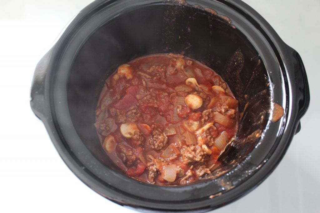 Beef and vegetable stew cooking in a black slow cooker.