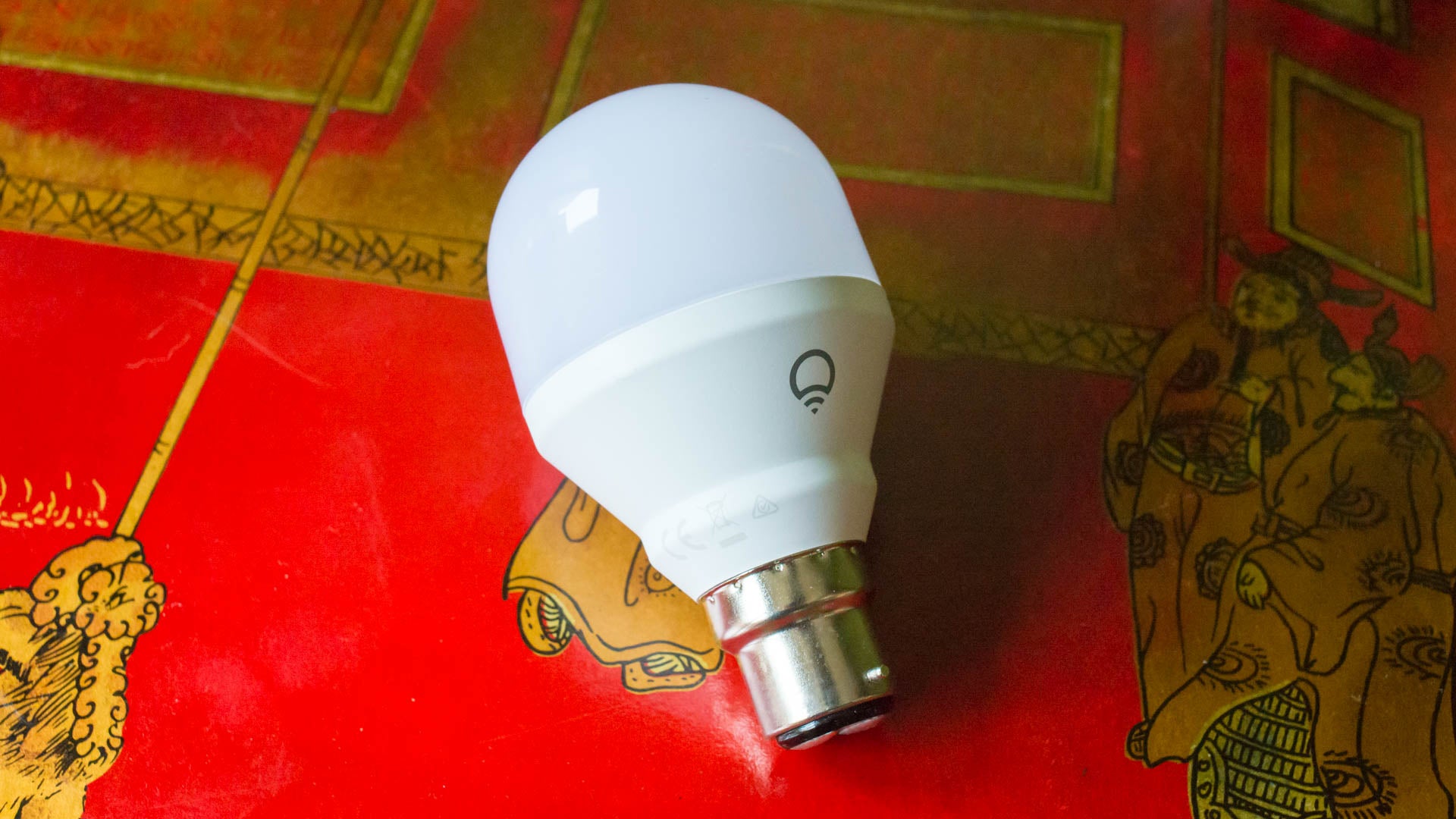LIFX Mini Smart Bulb on patterned red surface.