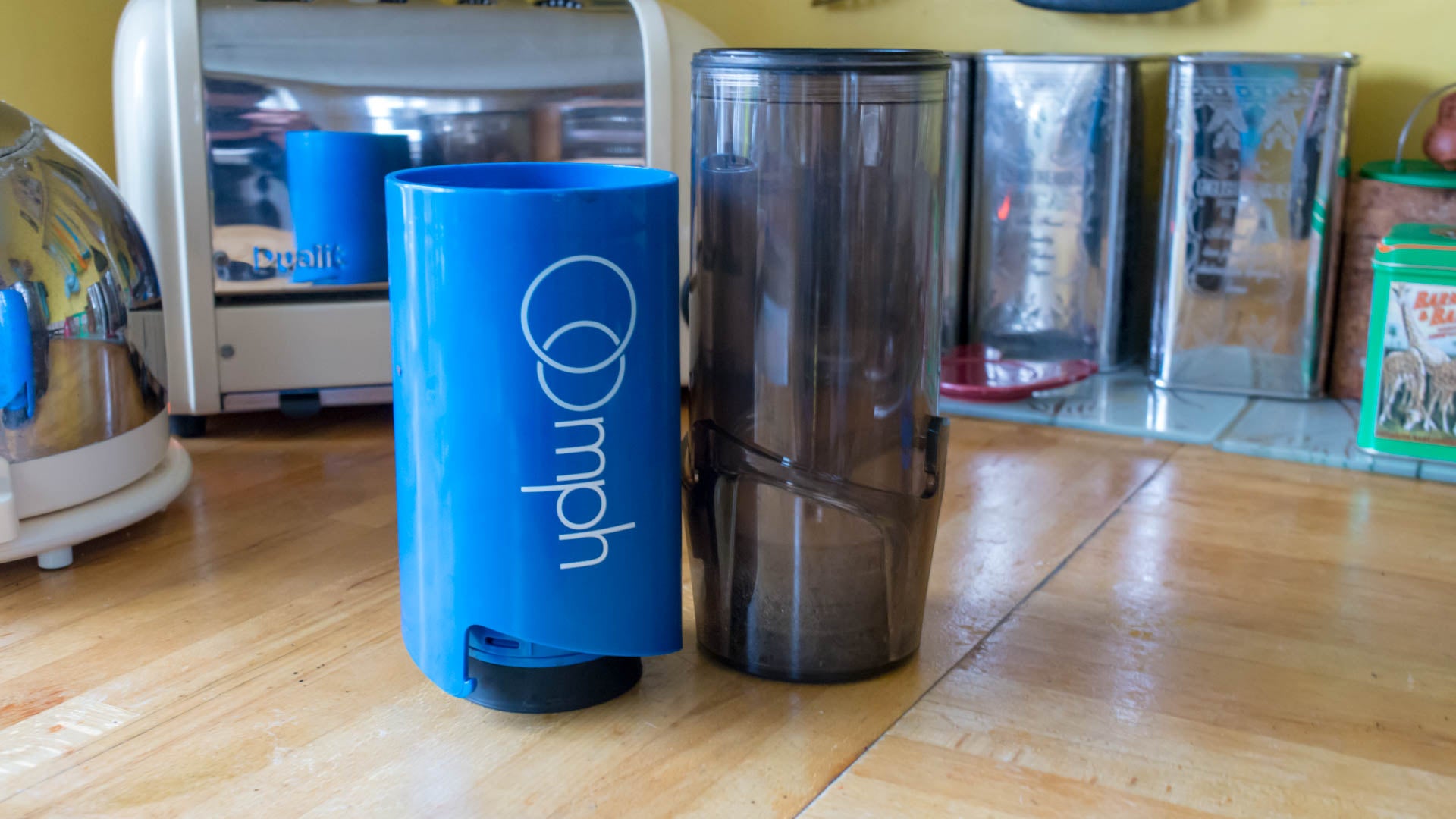 Blue Oomph Coffee Maker next to a clear coffee jug on a wooden counter.